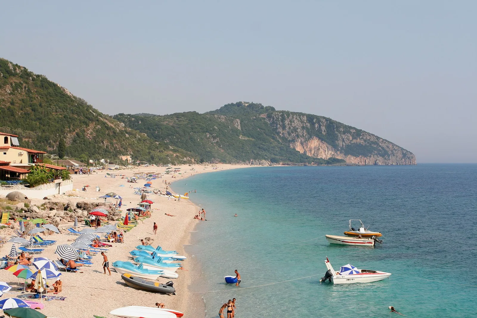 The long pebble beach of Dhermi with umbrellas, boats and green headlands on the Albanian Riviera