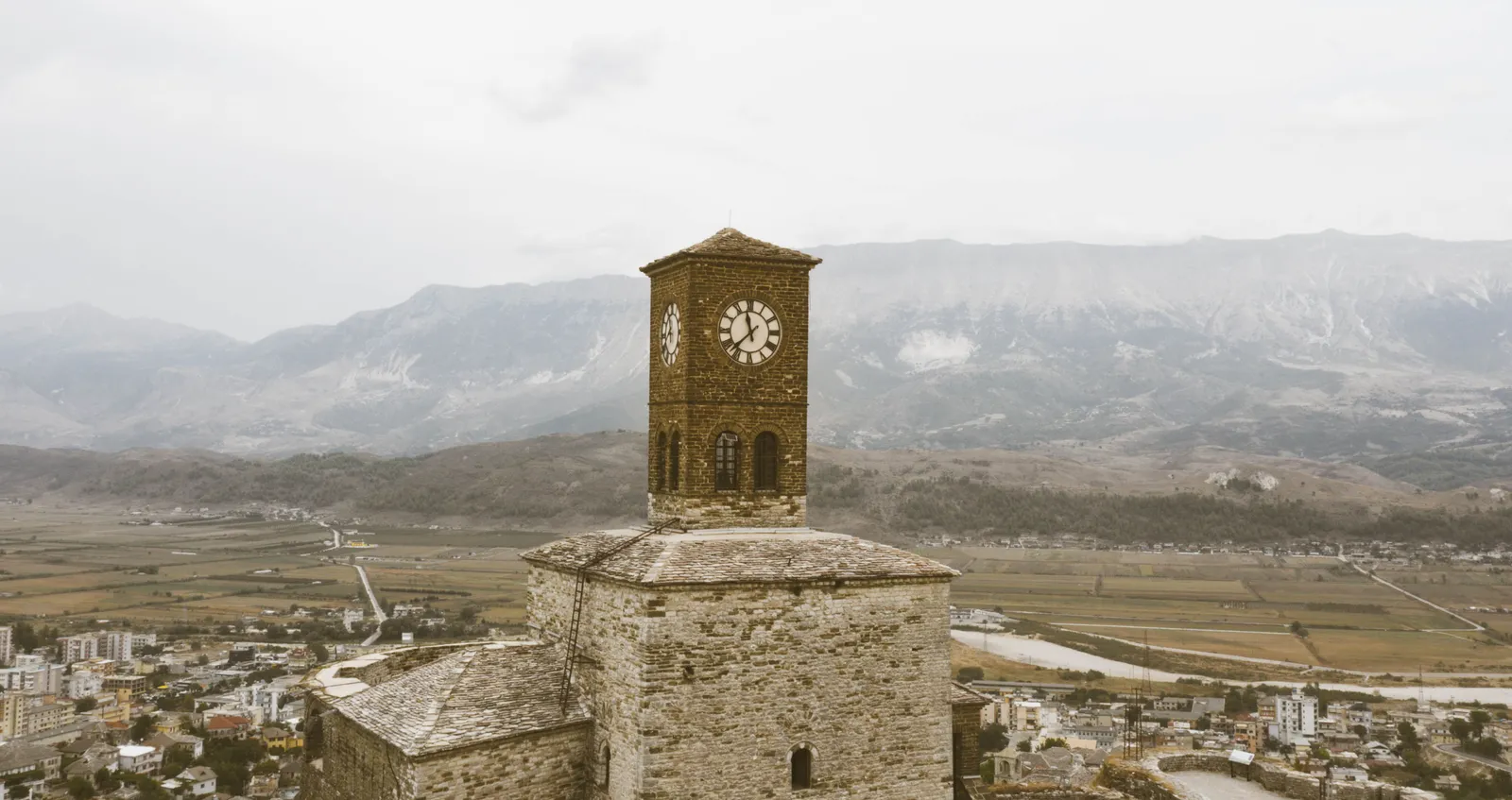 A clock tower on stone castle walls above a valley and mountains