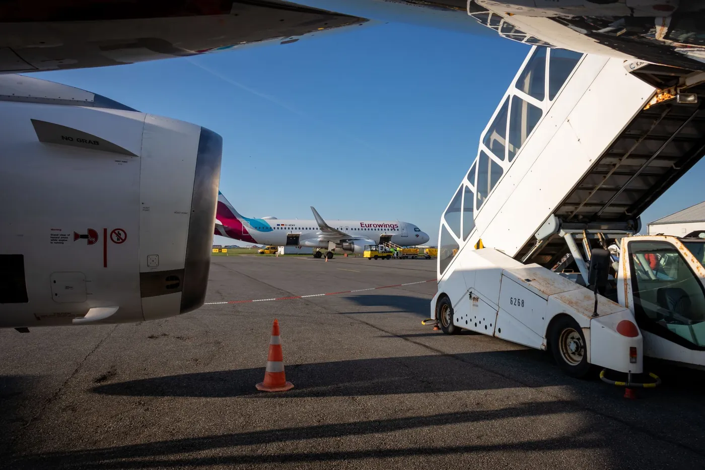 An airliner on the apron with boarding stairs beside an airport terminal in daylight