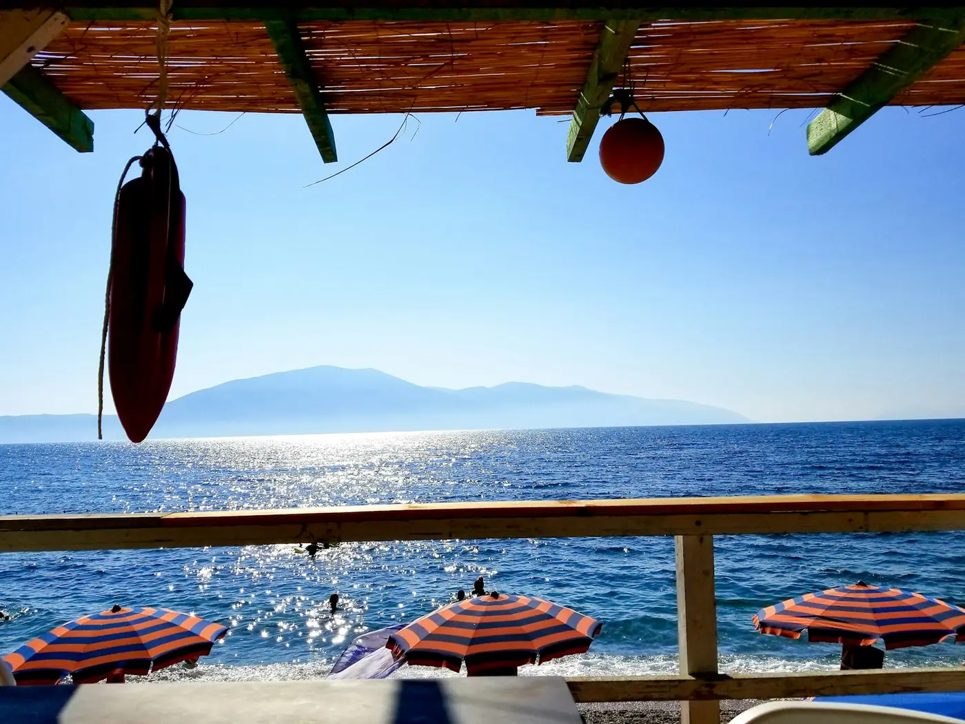 A shaded terrace looking out over the sea and beach umbrellas in daylight