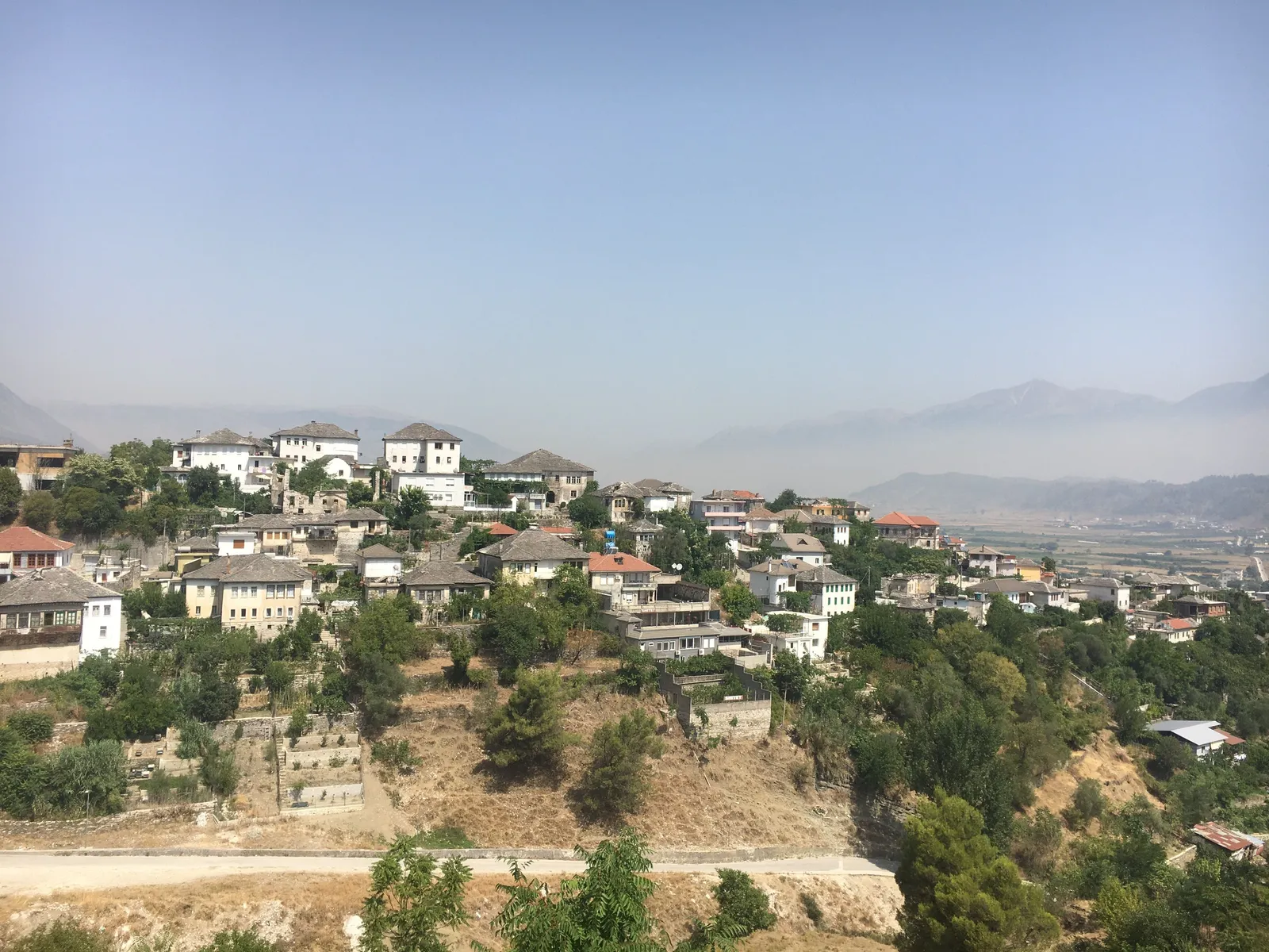 Stone houses of Gjirokaster spread across a hillside above an open valley and mountains in Albania