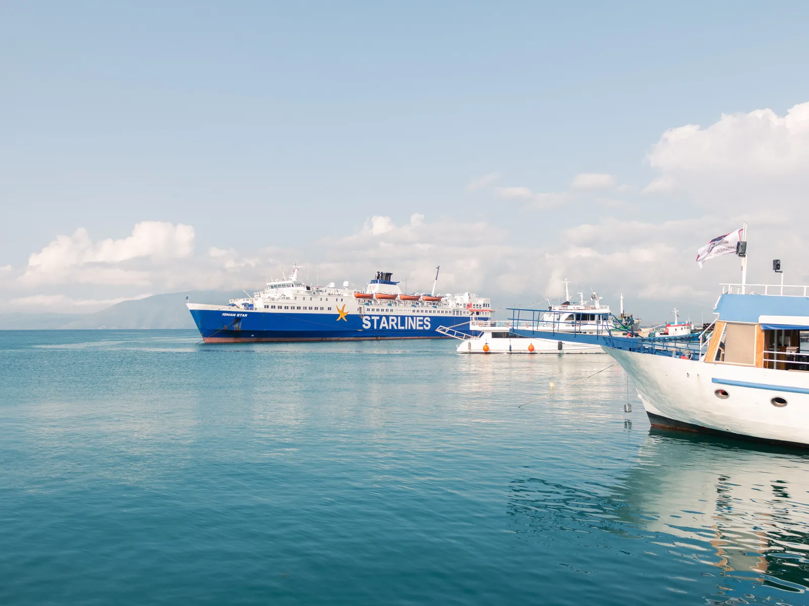 A Starlines car ferry moored in a calm Ionian bay on a clear day with smaller boats alongside