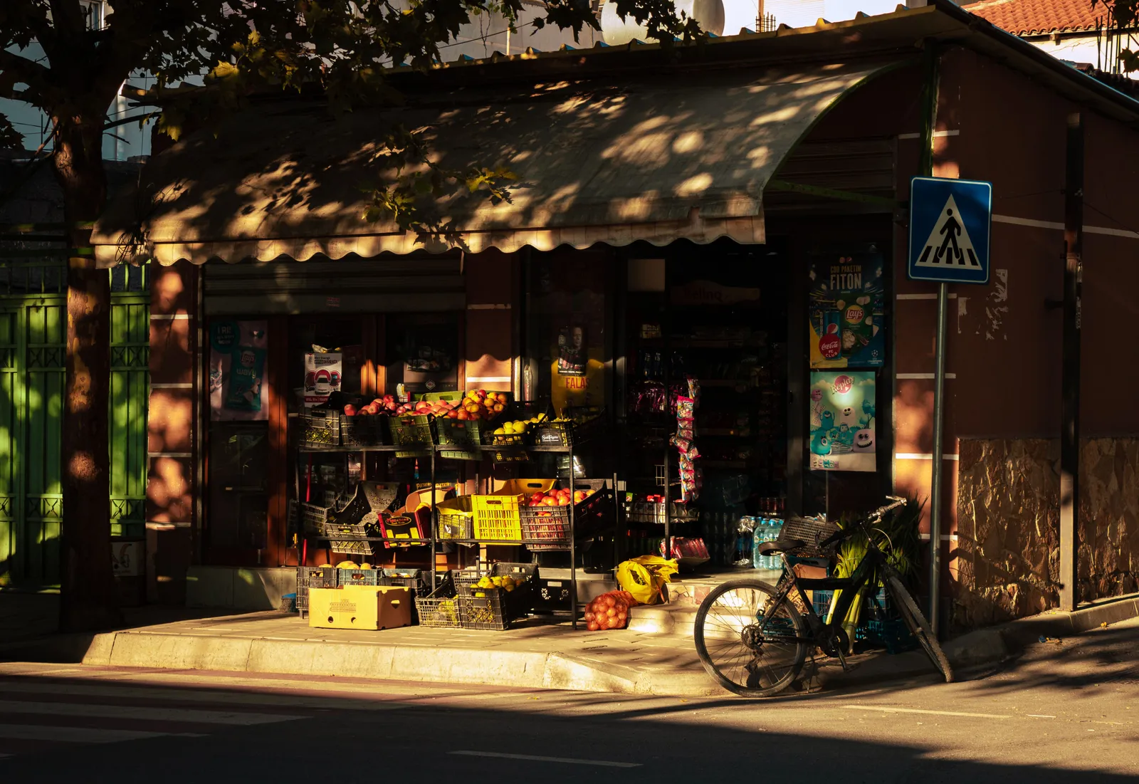 A small fruit and vegetable shop with crates of produce outside and a bicycle parked at the kerb in late afternoon sun