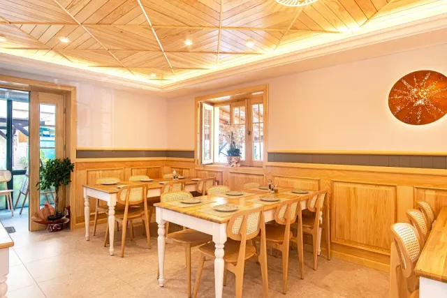 A bright dining room with a wooden ceiling, set tables and cane chairs by a window