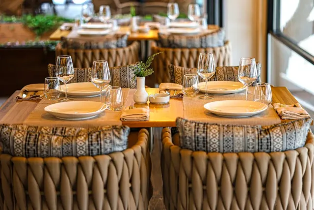 Wooden tables set with glasses and plates, woven armchairs and patterned cushions