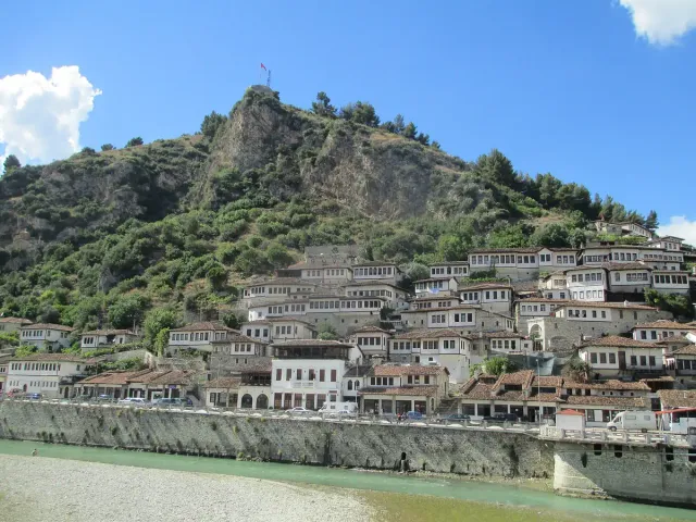 A steep slope covered with white stone houses full of windows beneath a green hill