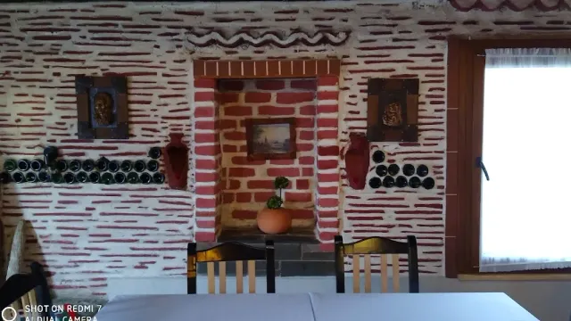 A red and white brick wall with a niche, rows of hanging bottles and a white table in front