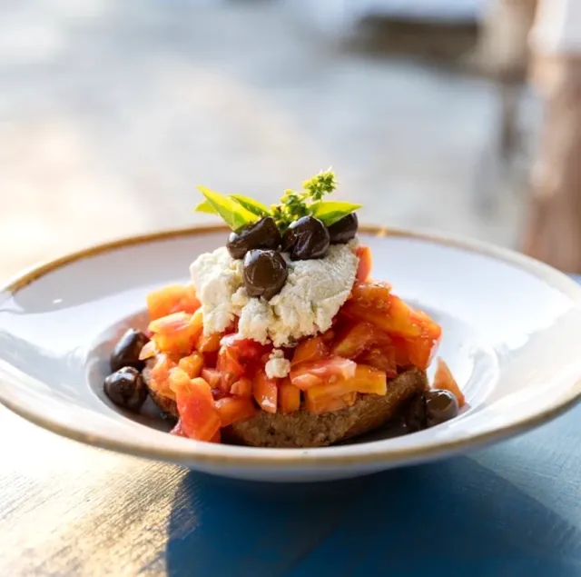 A slice of bread piled with chopped tomatoes, white cheese, black olives and a basil leaf