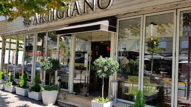 A glass front with a dark awning and olive trees in white pots along the sidewalk