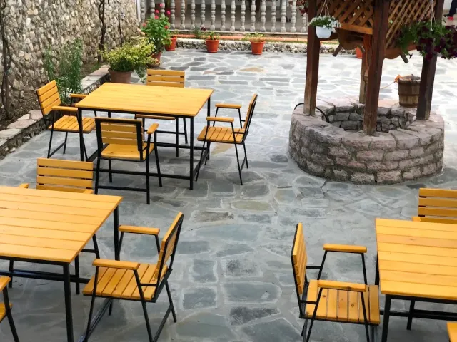 A stone paved courtyard with yellow wooden tables and chairs around a covered well
