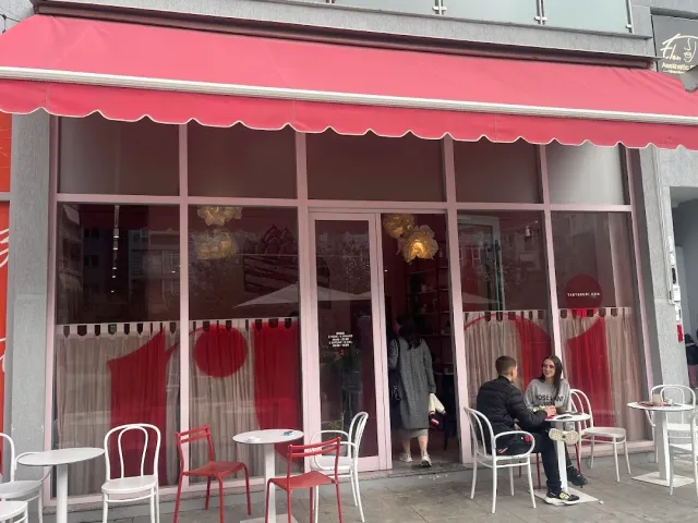 A cafe front with a red awning, shop windows and white and red chairs on the sidewalk