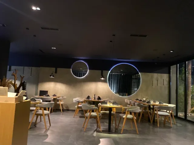 A dark designed room with lit round mirrors, wooden tables and light chairs
