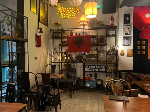 An interior full of objects with a metal shelving unit, a hanging flag, metal chairs and wooden tables