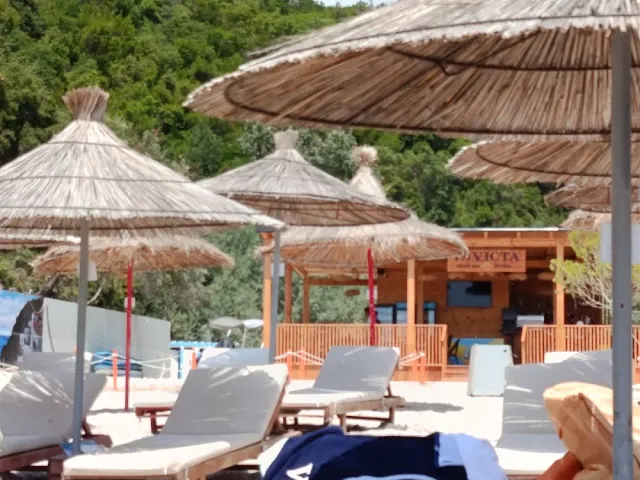 Straw parasols and sun loungers on a sandy beach, a wooden structure and a green hill behind