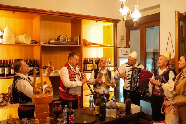 Six musicians in traditional dress and white felt caps playing accordion and drum