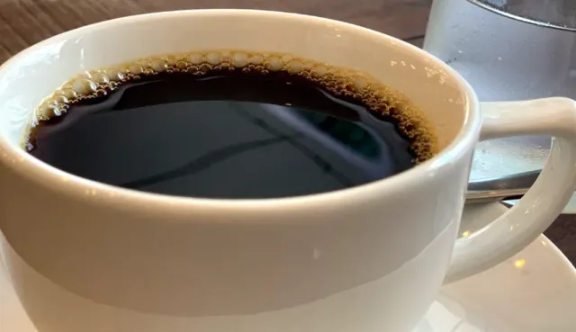 A close-up of a white cup filled with black coffee with a ring of bubbles at the rim