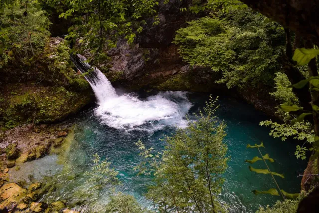 A white waterfall pouring into a turquoise pool surrounded by rocks and trees