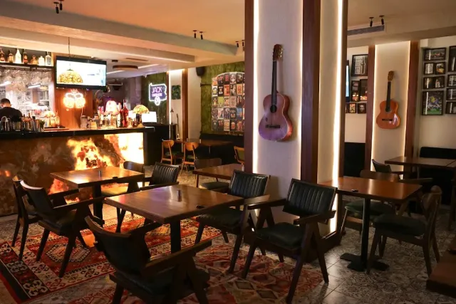 Wooden tables and dark leather armchairs, guitars hung on the wall and a fire burning behind