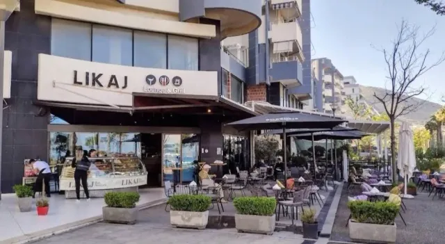 A shop frontage with a lit sign, a pastry display and a terrace with black parasols