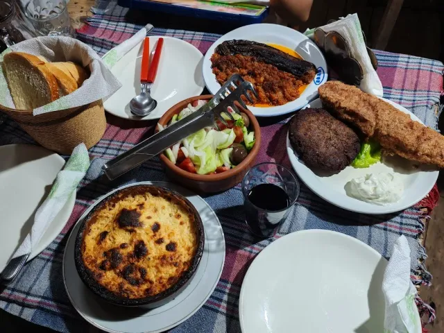 A table loaded with a bread basket, salad in a clay bowl, a baked casserole and a plate of patties
