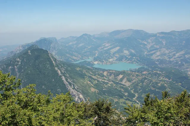 A turquoise reservoir winding between green mountain ridges, seen from above