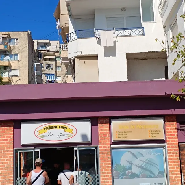 A low shop front with two signs, customers at the entrance and residential buildings behind