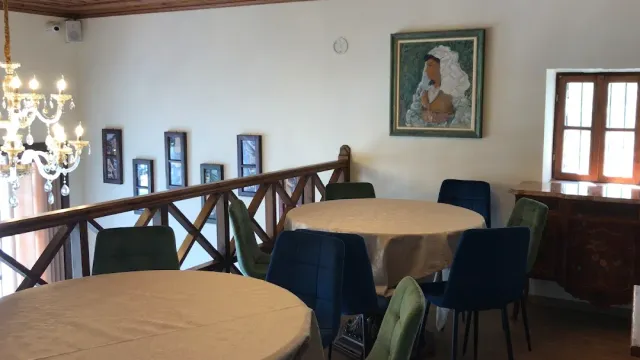 A dining room with round clothed tables, a crystal chandelier and a framed painting on the wall