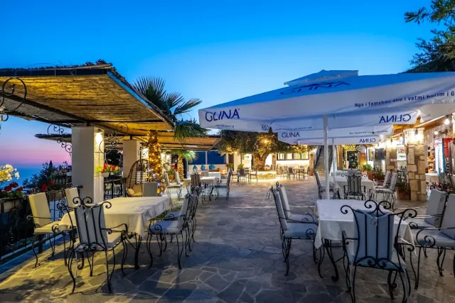 A paved terrace at dusk with white parasols, metal chairs and set tables