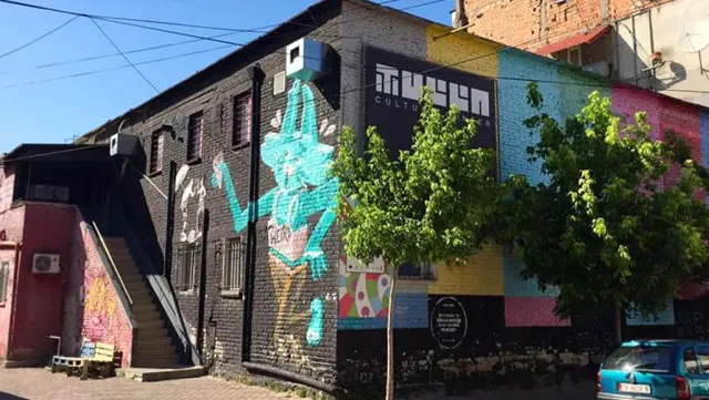 A black brick building with a colorful wall painting, an external metal staircase and trees
