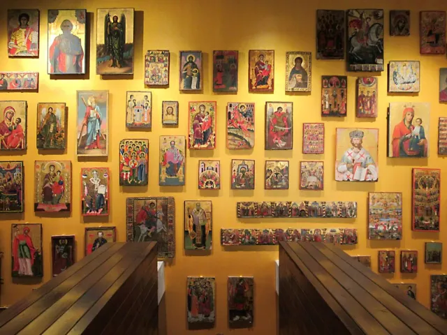 A yellow wall covered with dozens of Byzantine icons inside an exhibition hall