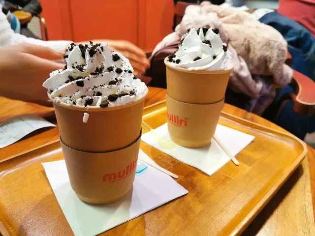 Two paper cups topped with whipped cream and chocolate flakes on a wooden tray