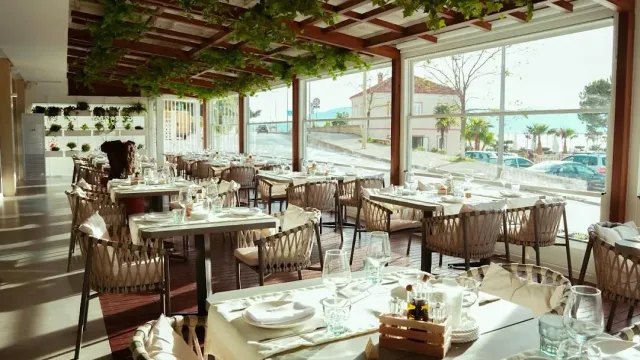 A glazed hall with a vine pergola, woven chairs and set tables facing windows