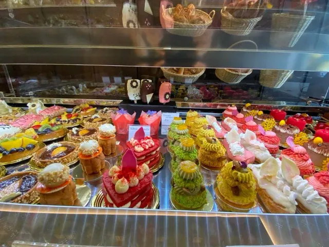A chilled display case packed with rows of colourful individual cakes, and pastry baskets above