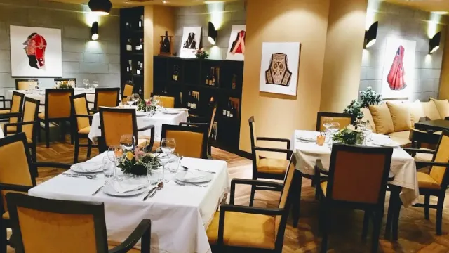A dining room with white cloths, mustard chairs and pictures of embroidered costumes on the walls