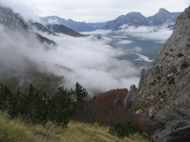Sharp rocky peaks above a valley filled with morning mist and forest