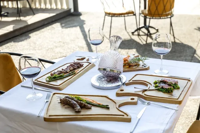 A white table with serving boards, plated dishes, glasses of red wine and a crystal decanter