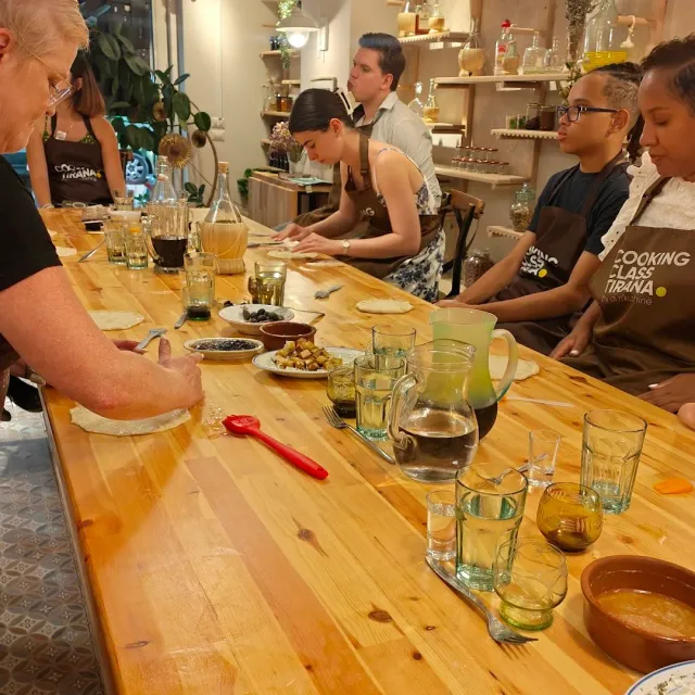 Participants in aprons rolling dough around a long wooden table with glasses and bowls