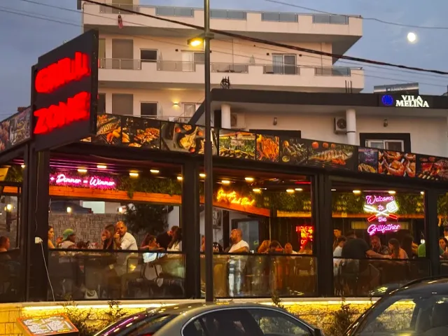 A terrace crowded in the evening with red neon letters and panels of dish photographs above