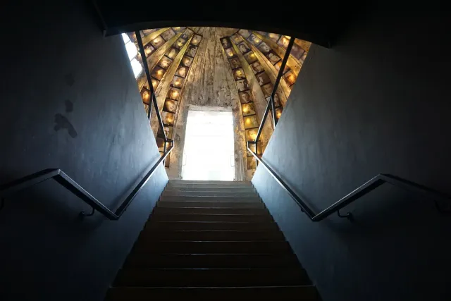 Concrete steps rising toward a bright doorway at the end of a tunnel lined with lamps