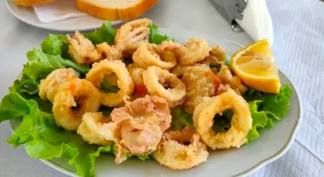 Fried calamari rings on a bed of green lettuce with a lemon wedge on a white plate