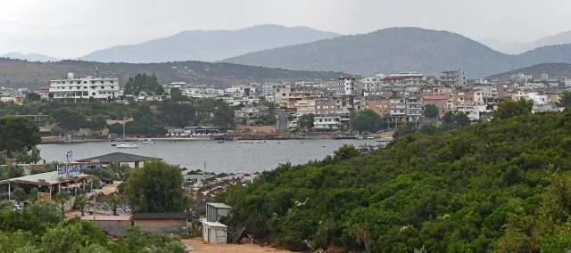 A view from a wooded hill over a bay and the town houses beyond it, with hazy mountains