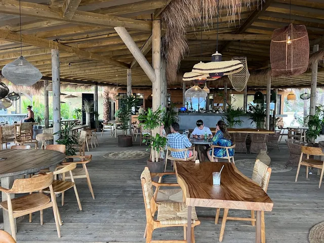 An open wooden pavilion with a thatched roof, solid wood tables and woven hanging lamps