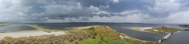 A grassy spit reaching into a shallow lagoon under dramatic cloudy skies