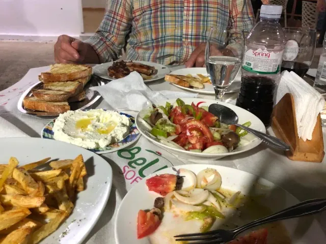 A table loaded with plates of fries, toasted bread, tomato salad and a white cheese spread