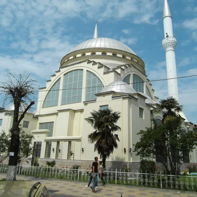 A white mosque with a large dome and a tall minaret among palm trees