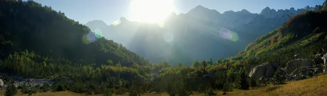 A wide valley panorama with forested slopes and sunlit alpine peaks