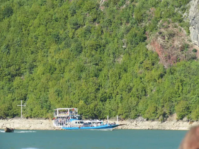 A small ferry on green water between steep cliffs covered in vegetation