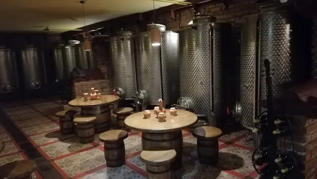 A cellar with stainless steel wine tanks, round tables and wooden barrel stools