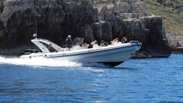 A rigid inflatable boat with passengers speeding past rock cliffs