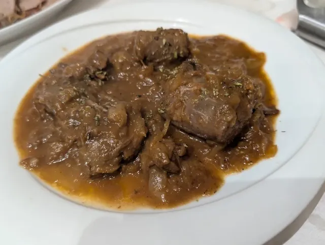 A white plate with chunks of meat in a thick brown sauce and fried onion